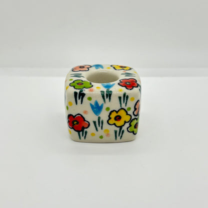 Side profile view of a Ceramika Artystyczna Polish pottery cube-shaped taper candle holder showing the cuboid block, top candle socket, and hand-painted spring flowers.