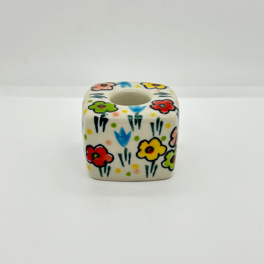 Side profile view of a Ceramika Artystyczna Polish pottery cube-shaped taper candle holder showing the cuboid block, top candle socket, and hand-painted spring flowers.