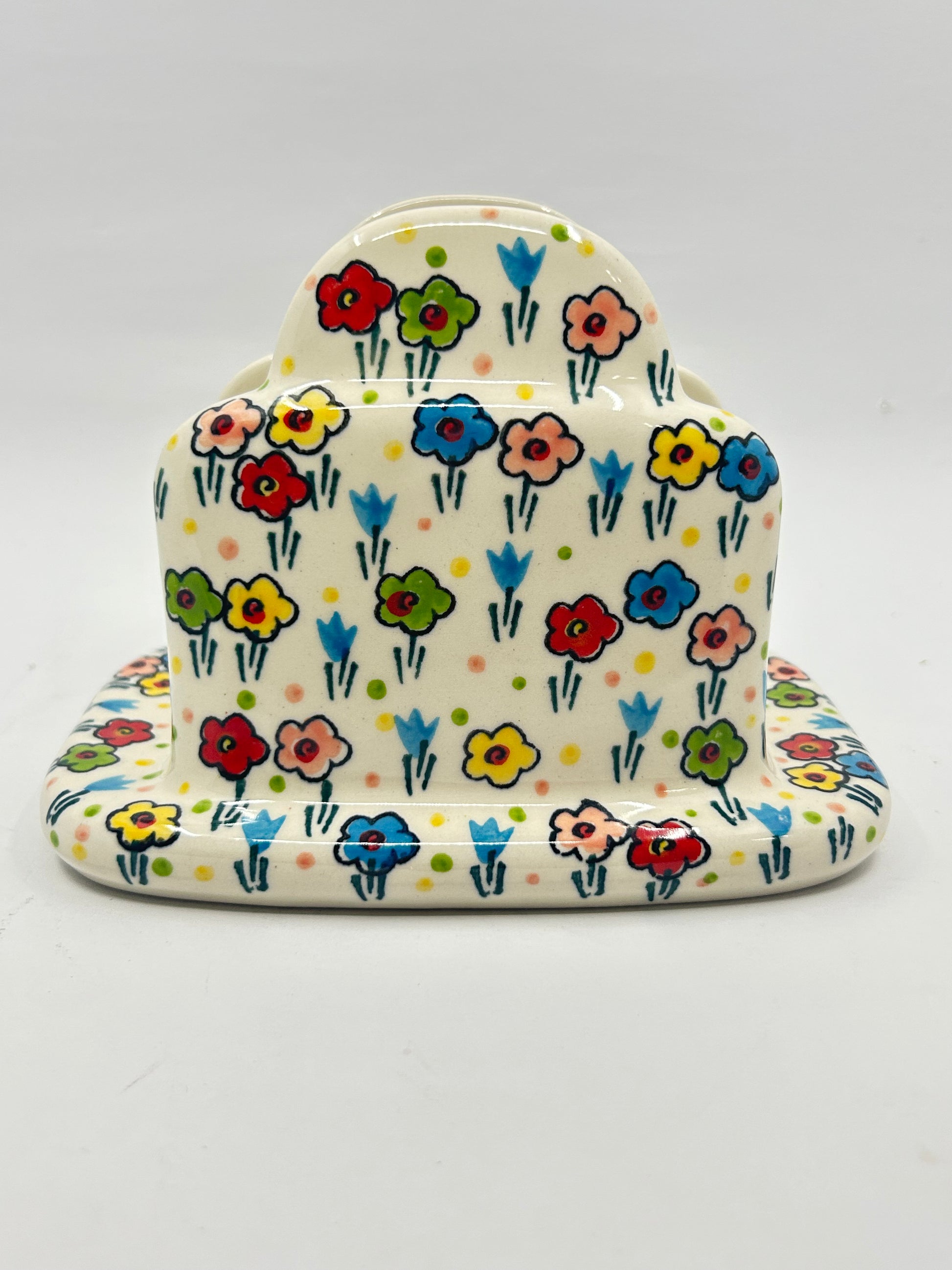 Front-facing view of a Ceramika Artystyczna Polish pottery napkin holder featuring a tiered upright design and hand-painted multi-colored spring flowers covering the entire surface.