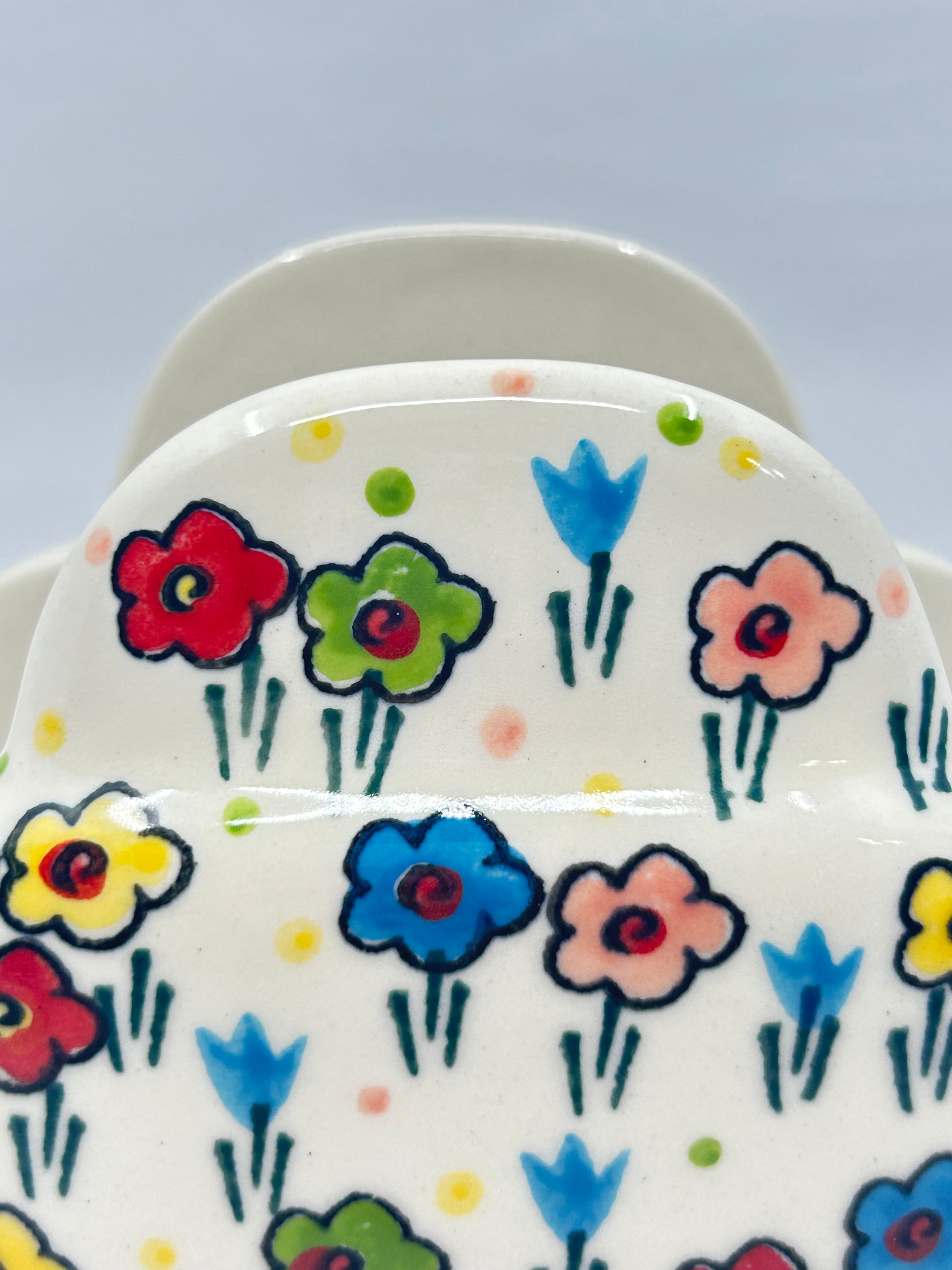Macro close-up of a Ceramika Artystyczna Polish pottery napkin holder showing hand-painted spring flowers with bold outlines, green stems, and a glossy glaze.