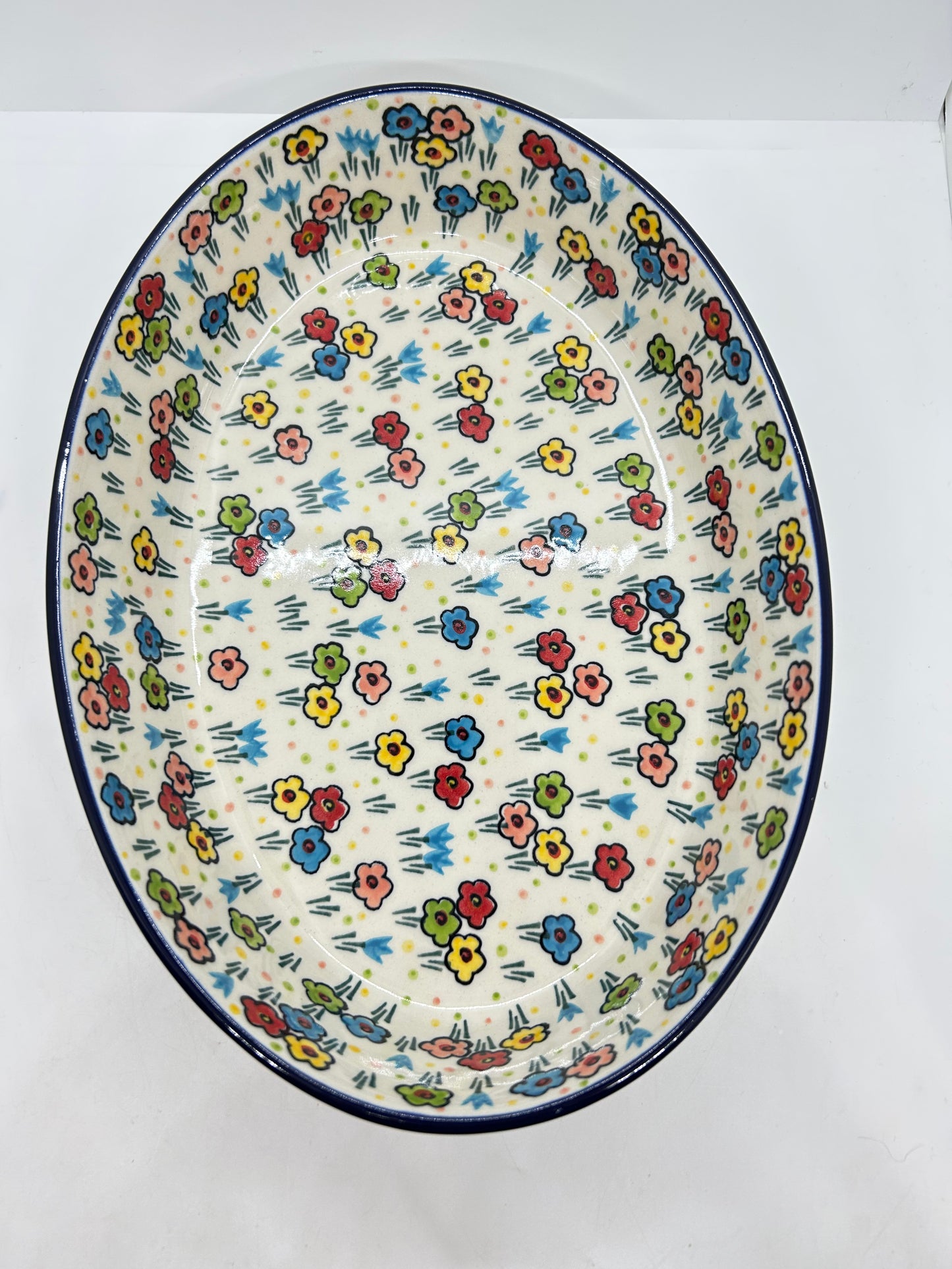 Direct overhead view looking into a Ceramika Artystyczna Polish pottery oval baker, showing a continuous dark blue rim and a vast, fully decorated interior basin featuring hand-painted multi-colored spring flowers.