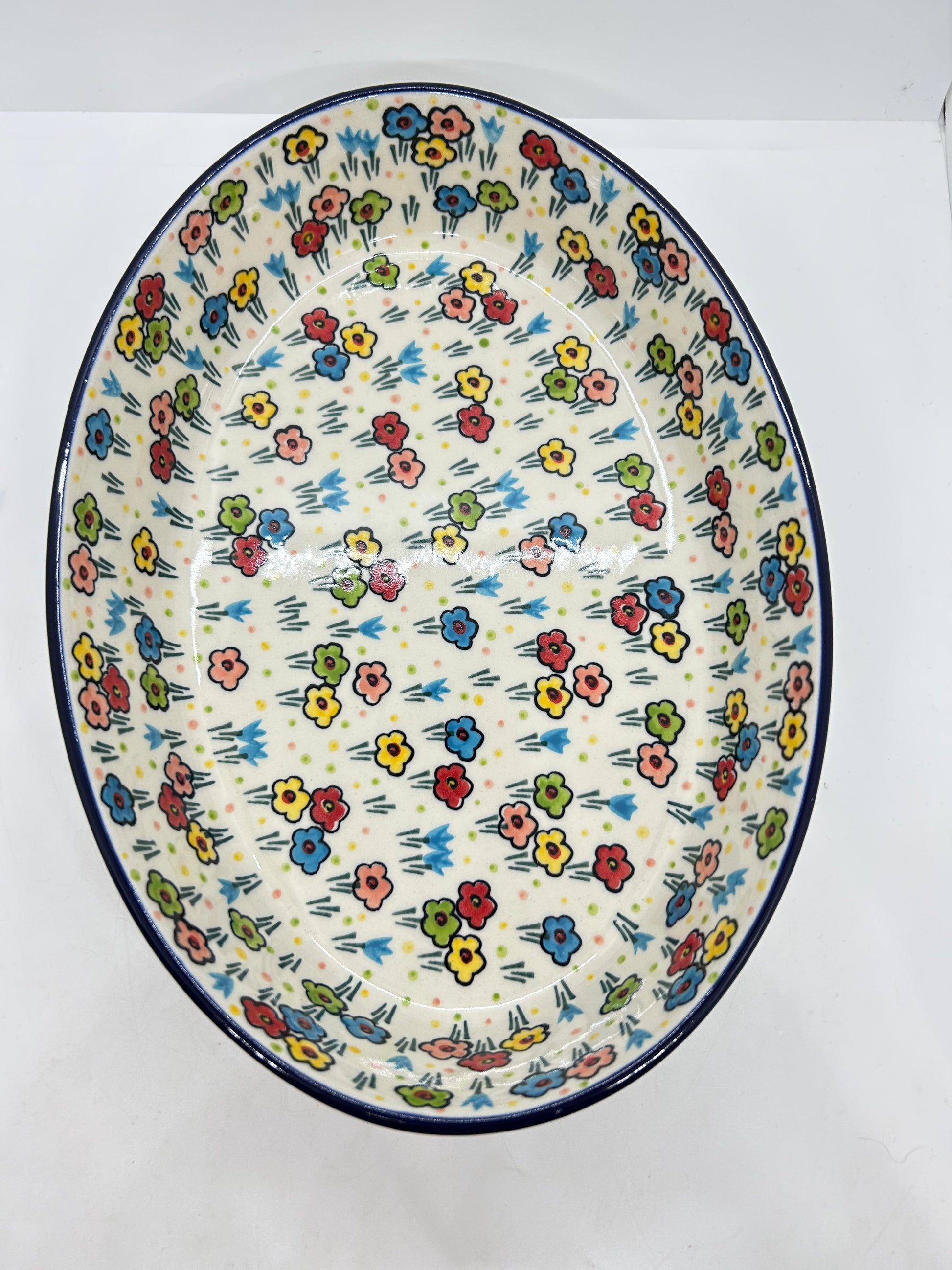 Direct overhead view looking into a Ceramika Artystyczna Polish pottery oval baker, showing a continuous dark blue rim and a vast, fully decorated interior basin featuring hand-painted multi-colored spring flowers.