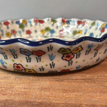 Extreme close-up of the fluted exterior wall of a Ceramika Artystyczna Polish pottery quiche dish resting on wood, highlighting the wavy dark blue rim and hand-painted multi-colored spring flowers.