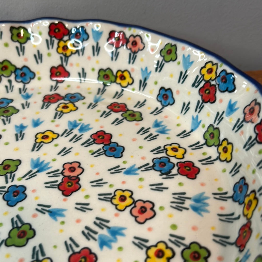 Extreme close-up of the interior basin of a Ceramika Artystyczna Polish pottery quiche dish, showing high-gloss reflections and hand-painted multi-colored spring flowers radiating inward.