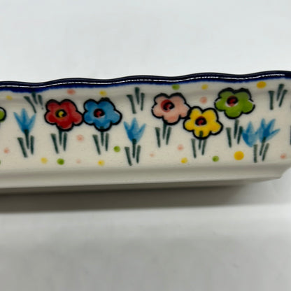 Macro close-up of the exterior wall of a Ceramika Artystyczna Polish pottery rectangular tray showing hand-painted spring flowers, green stems, and a dark blue rim.
