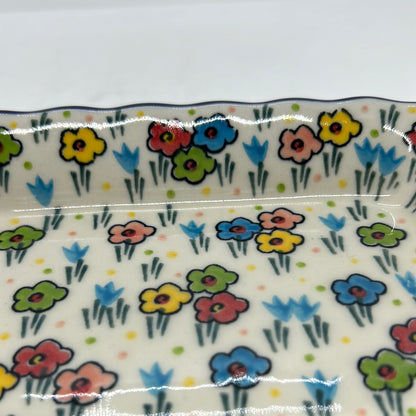 Macro close-up of a Ceramika Artystyczna Polish pottery rectangular serving tray, showing hand-painted spring flowers with bold outlines, green stems, and a glossy protective glaze.