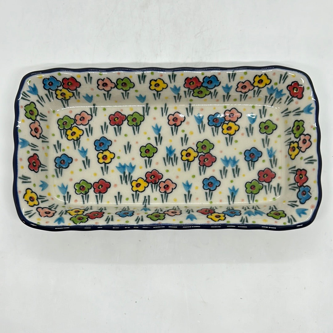 Direct overhead view of a Ceramika Artystyczna Polish pottery rectangular serving tray, showing a wavy dark blue rim and hand-painted multi-colored spring flowers across the flat interior basin.