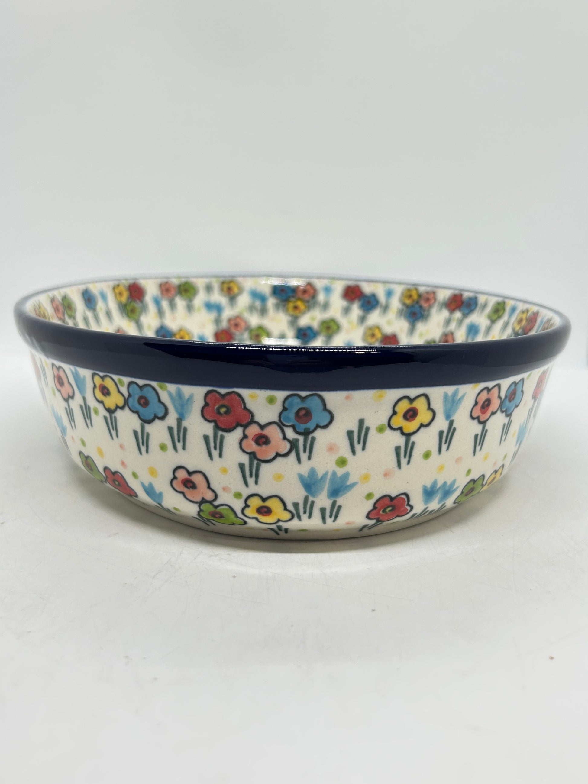 Straight-on side profile of a Ceramika Artystyczna Polish pottery round baker, highlighting a thick dark blue upper rim and hand-painted multi-colored spring flowers on the upright exterior walls.