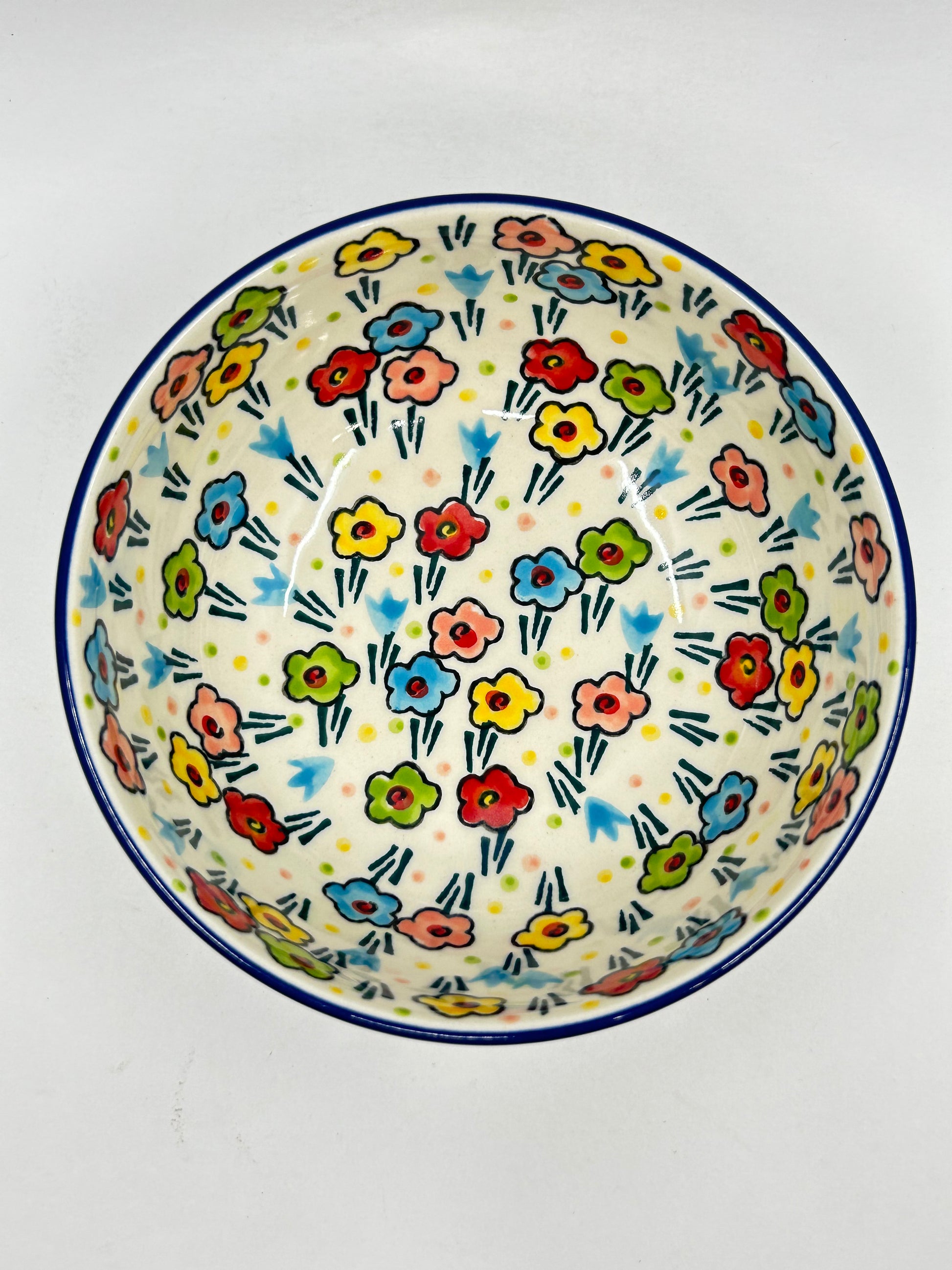 Direct overhead view looking inside a Ceramika Artystyczna Polish pottery round serving bowl, showing a dark blue rim and a symmetrical layout of hand-painted multi-colored spring flowers across the cream-colored interior basin.