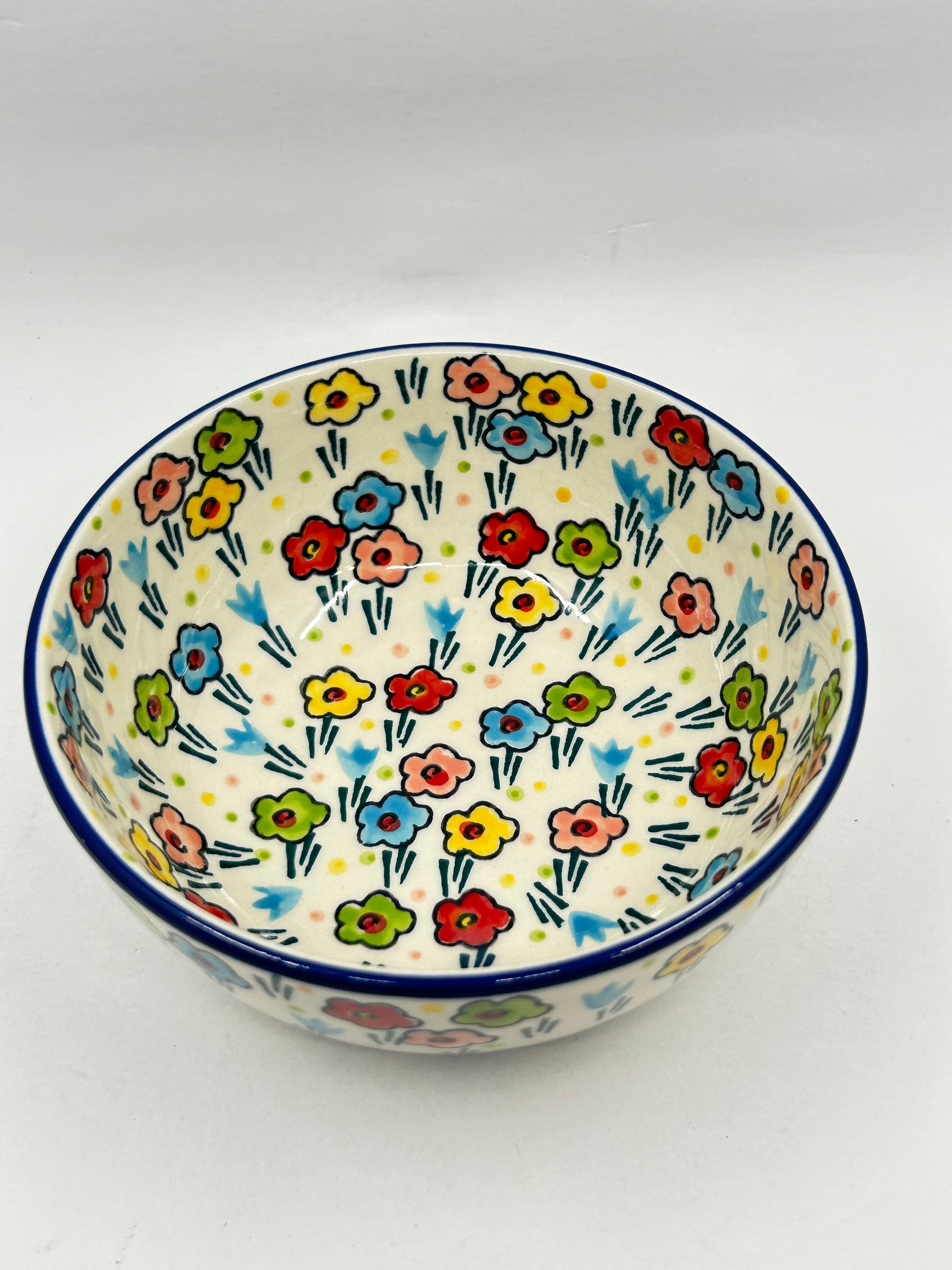 Elevated high-angle view of a Ceramika Artystyczna Polish pottery round serving bowl, showing a dark blue rim and hand-painted multi-colored spring flowers covering the interior and exterior.