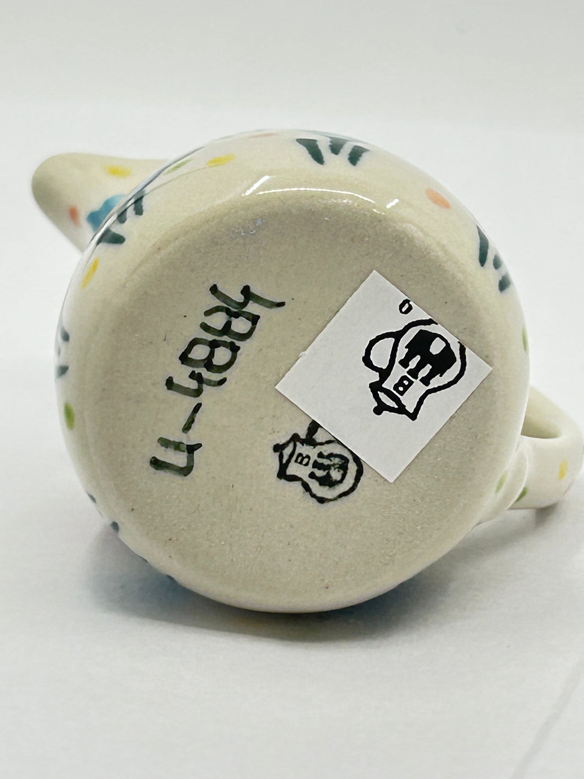 Close-up of the unglazed base of a Ceramika Artystyczna creamer pitcher showing the T. Liana UNIKAT 4884 signature and the Bolesławiec factory stamp.