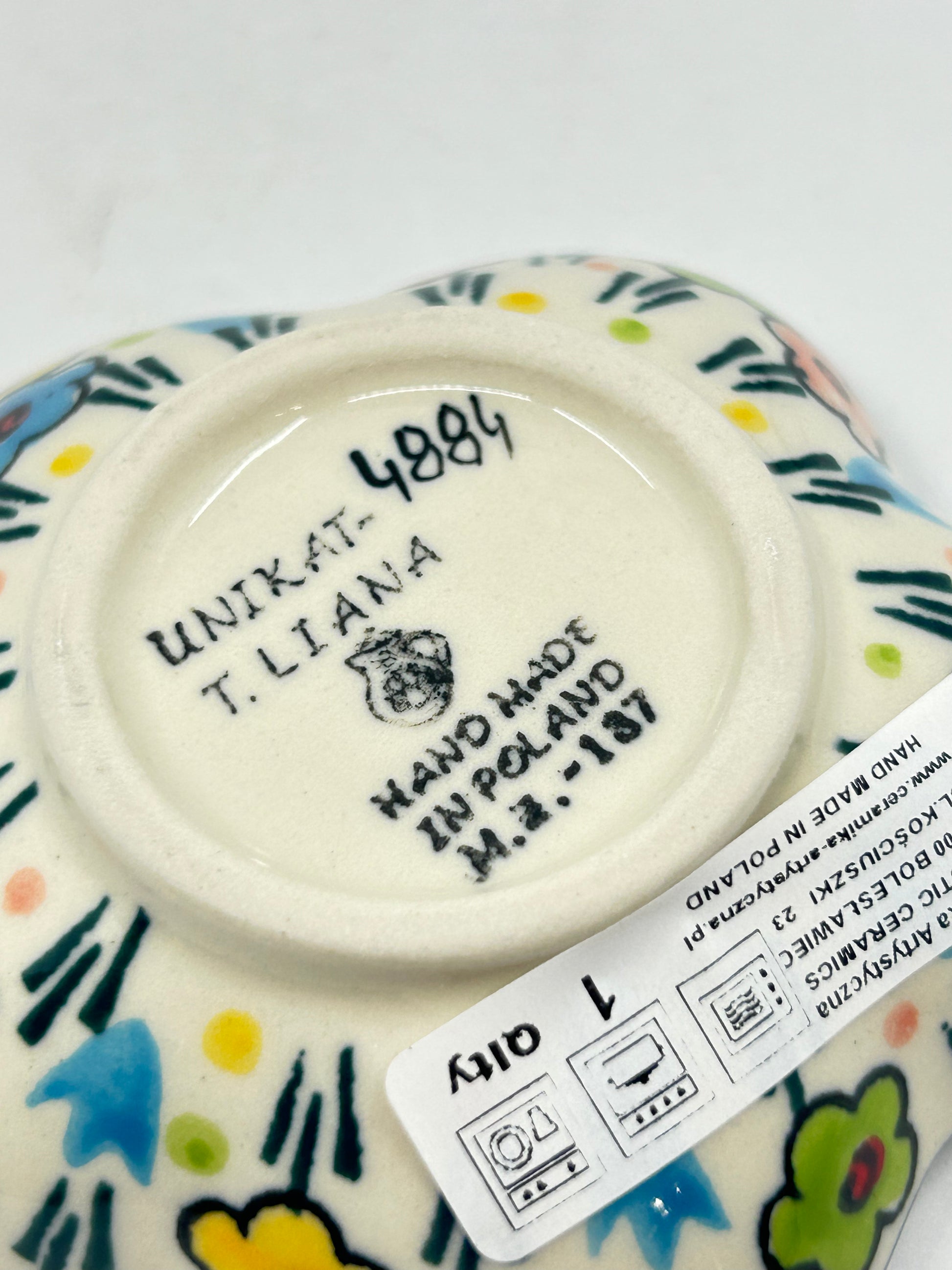Close-up of the unglazed base of a Ceramika Artystyczna flower-shaped dish showing the T. Liana UNIKAT 4884 signature and the Bolesławiec factory stamp.