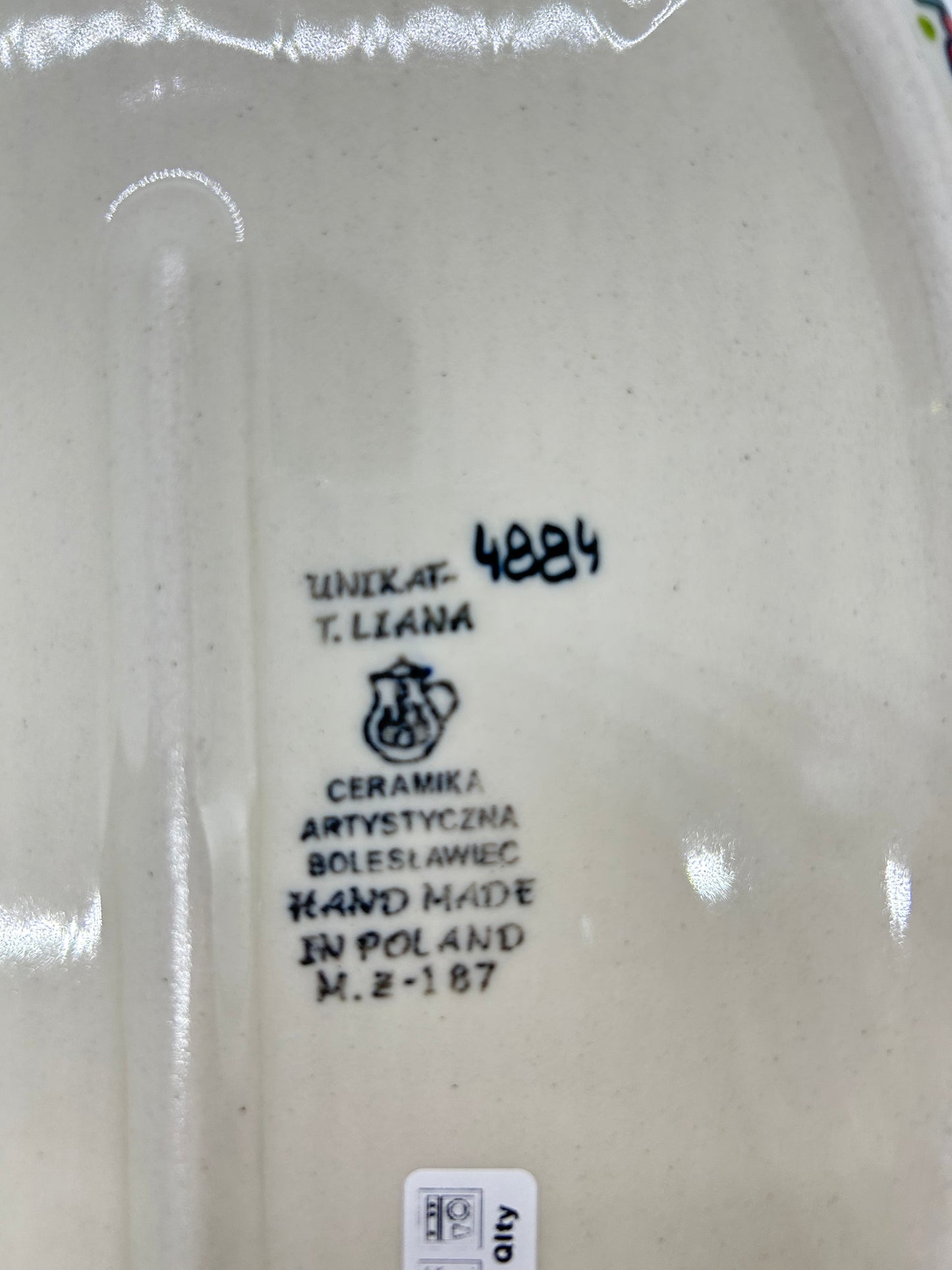 Close-up of the unglazed base of a Ceramika Artystyczna oval baker showin the T. Liana UNIKAT 4884 signature and a partial first-quality factory sticker.
