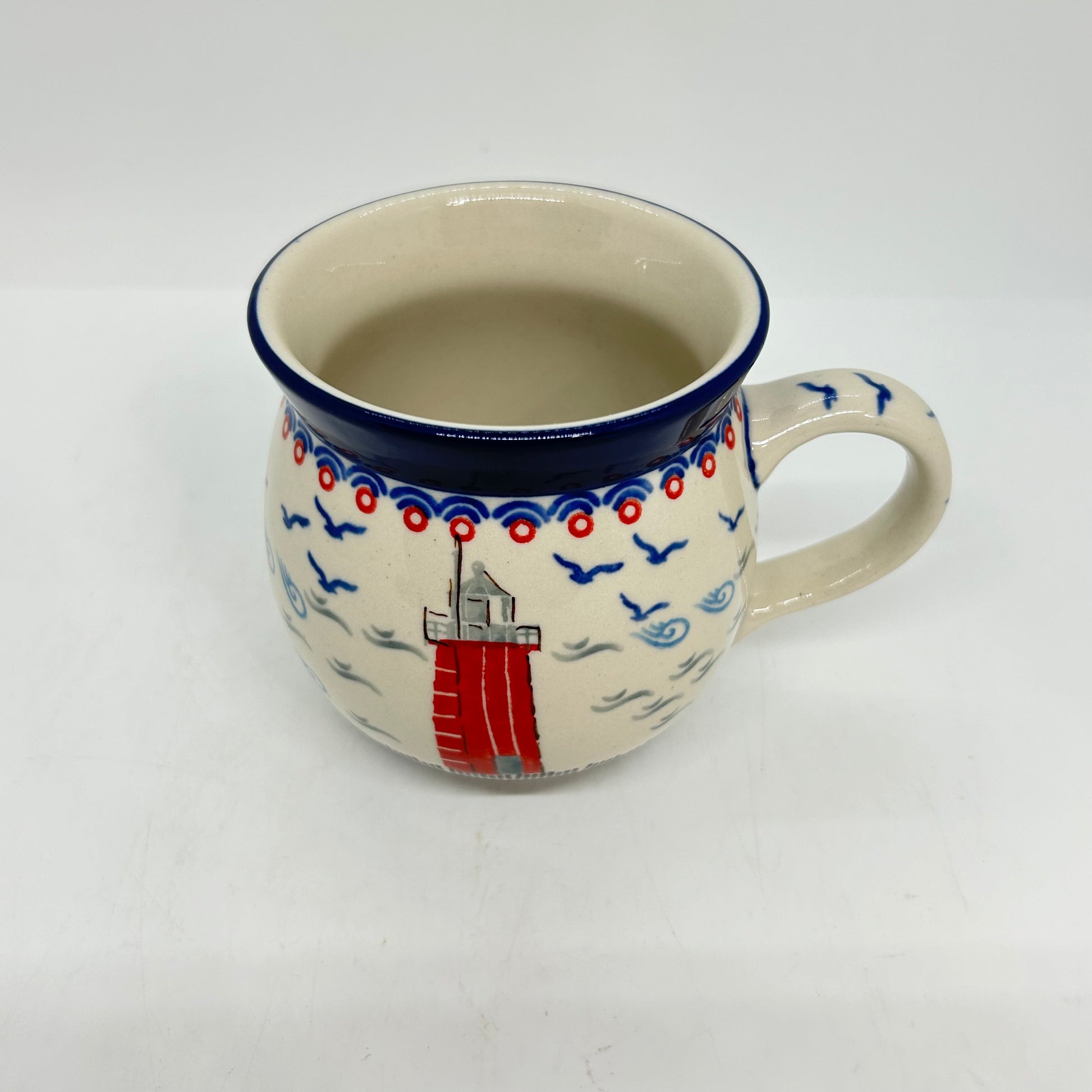Angled top-down view of an 11oz Ceramika Artystyczna Polish pottery bubble mug in the Unikat U5164 pattern, showing the lighthouse exterior, the wide blue lip, and a clean, undecorated interior.