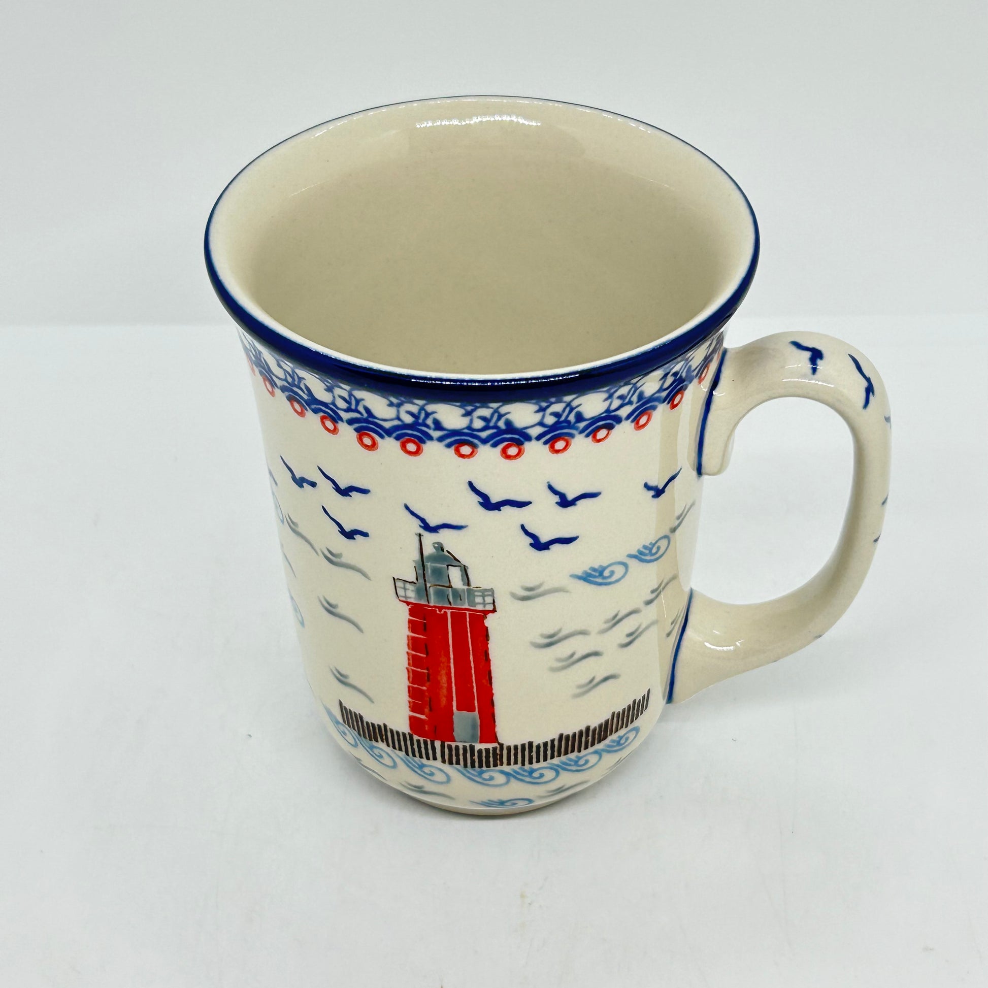Angled top-down view of a large 16oz Ceramika Artystyczna Polish pottery bistro mug in the Unikat U5164 pattern, showing the lighthouse exterior, blue rim, and the interior.