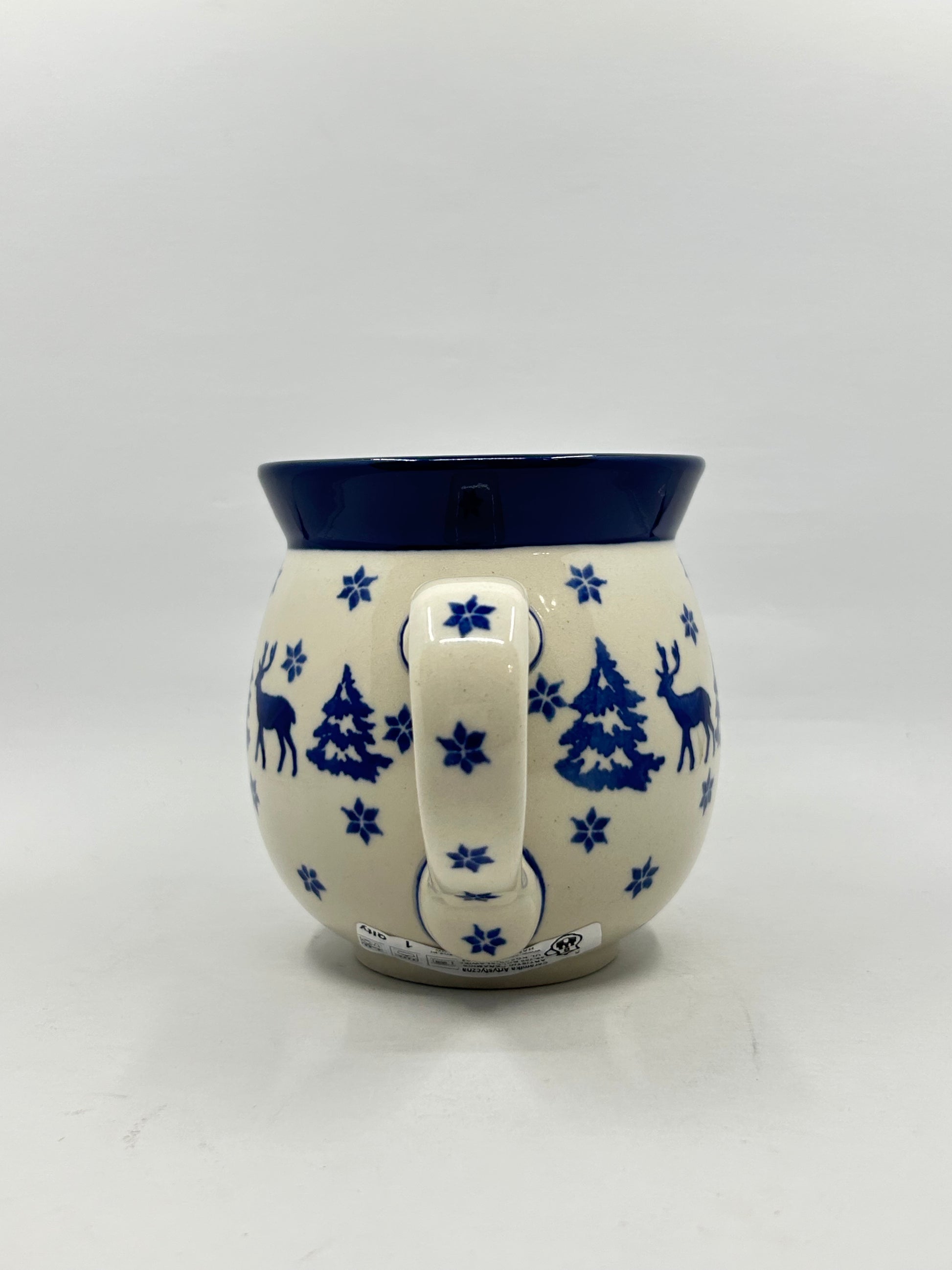 Straight-on view focusing on the patterned handle of a Ceramika Artystyczna Polish pottery bubble mug, flanked by pine trees, snowflakes, and a solid dark blue rim.