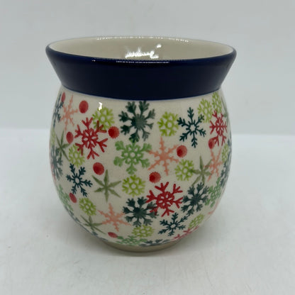 Straight-on view of the back of a Ceramika Artystyczna Polish pottery bubble mug, showing a continuous pattern of red, green, and pink snowflakes, scattered red dots, and a solid dark blue rim with no handle visible.
