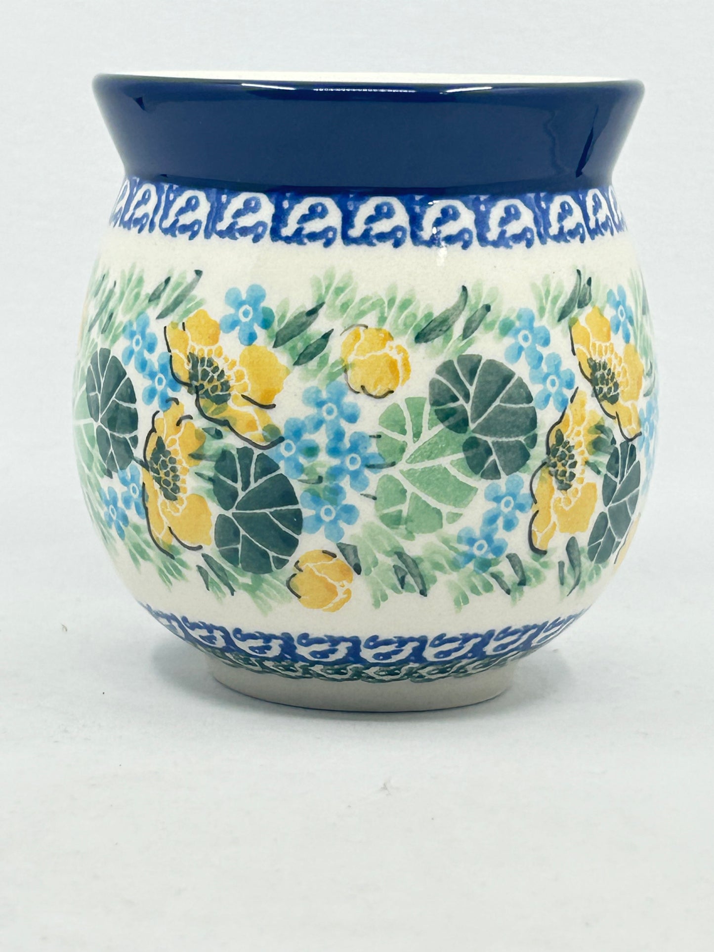 Straight-on view of the back of a Ceramika Artystyczna Polish pottery bubble mug, showing a continuous pattern of yellow and blue flowers, patterned borders, and a solid dark blue rim with no handle visible.