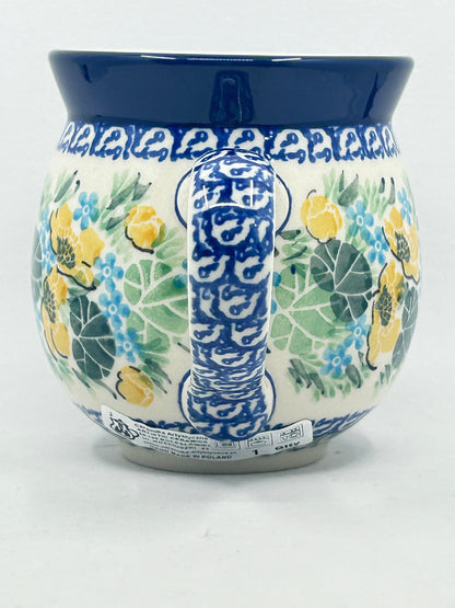 Straight-on view focusing on the intricately patterned blue and white handle of a Ceramika Artystyczna Polish pottery bubble mug, flanked by yellow and blue hand-painted flowers, green leaves, and a solid dark blue rim.