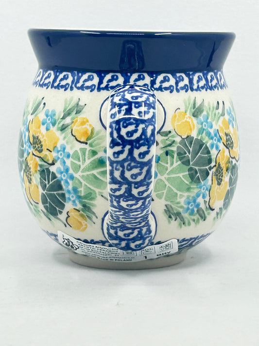 Straight-on view focusing on the intricately patterned blue and white handle of a Ceramika Artystyczna Polish pottery bubble mug, flanked by yellow and blue hand-painted flowers, green leaves, and a solid dark blue rim.