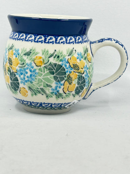 Straight-on side profile of a Ceramika Artystyczna Polish pottery bubble mug with the handle on the right, featuring hand-painted yellow and blue flowers, lush green leaves, patterned borders, and a solid dark blue rim.
