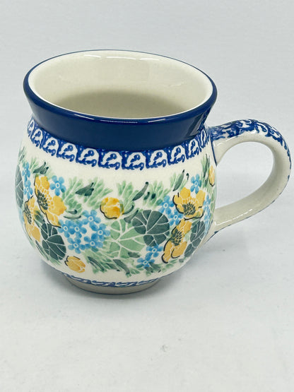 Elevated three-quarter view of a Ceramika Artystyczna Polish pottery bubble mug featuring hand-painted yellow and blue flowers, green leaves, patterned borders, a patterned right handle, and a smooth off-white interior.