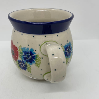 Elevated profile view of a Ceramika Artystyczna Polish pottery bubble mug, focusing on the dotted right handle, hand-painted blue cornflowers, a red poppy, and a solid dark blue rim.