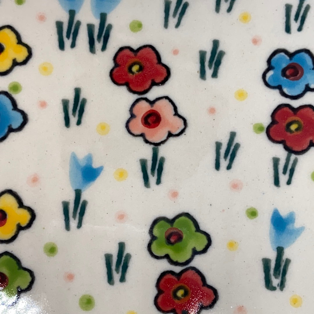 Extreme close-up of a Ceramika Artystyczna Polish pottery plate showing high-gloss glaze over hand-painted multi-colored flowers, light blue buds, and scattered dots.