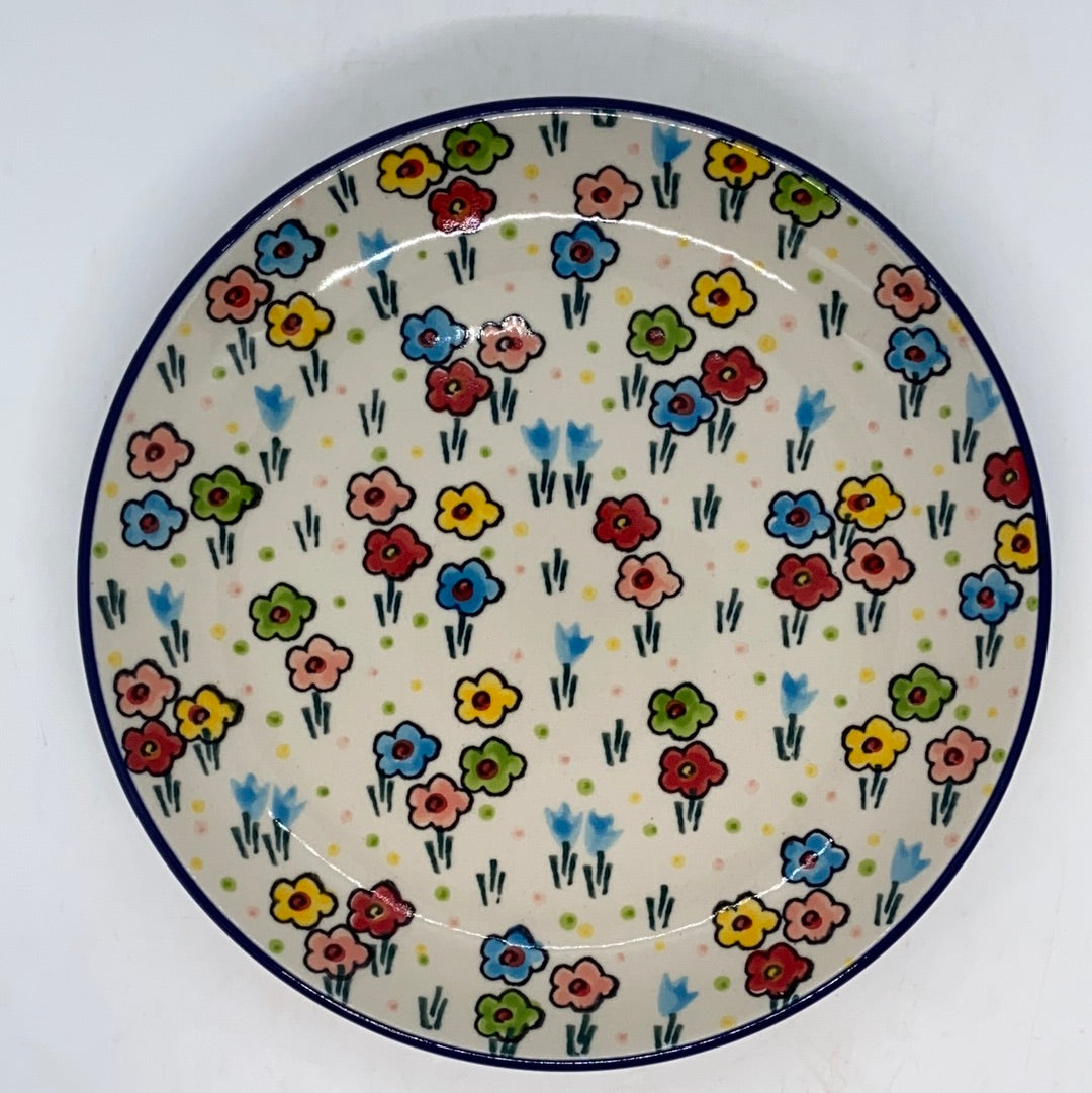 Overhead top-down view of a Ceramika Artystyczna Polish pottery plate covered in scattered, multi-colored hand-painted flowers, light blue buds, and a thin dark blue rim.   