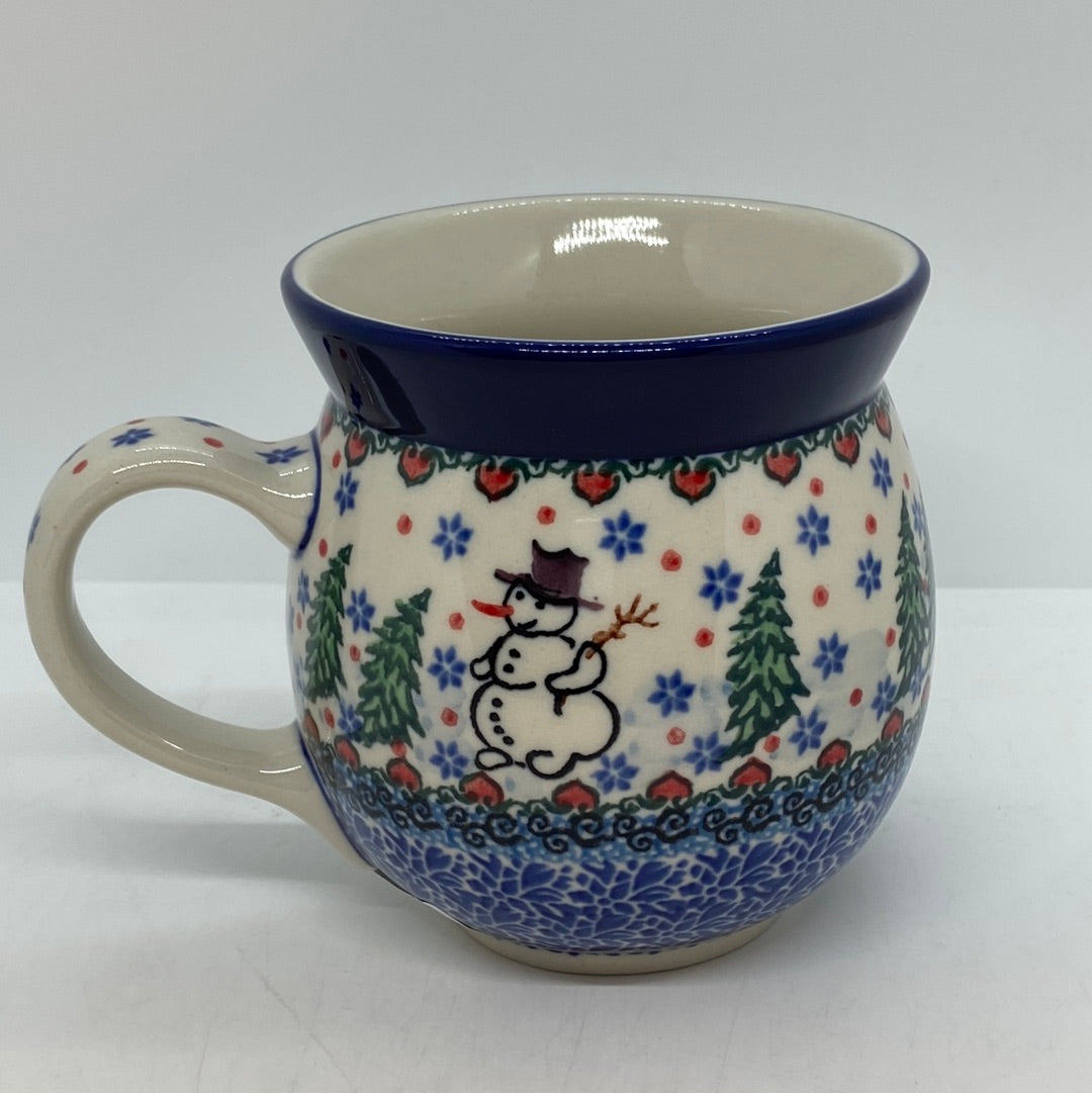 Straight-on side profile of a Ceramika Artystyczna Polish pottery bubble mug with the handle on the left, featuring a hand-painted snowman, green pine trees, blue snowflakes, and a solid dark blue rim.