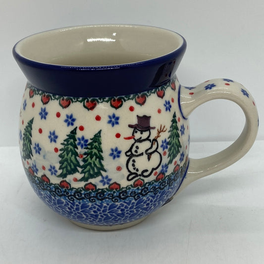 Straight-on side profile of a Ceramika Artystyczna Polish pottery bubble mug with the handle on the right, featuring a hand-painted snowman, green pine trees, blue snowflakes, and a solid dark blue rim.
