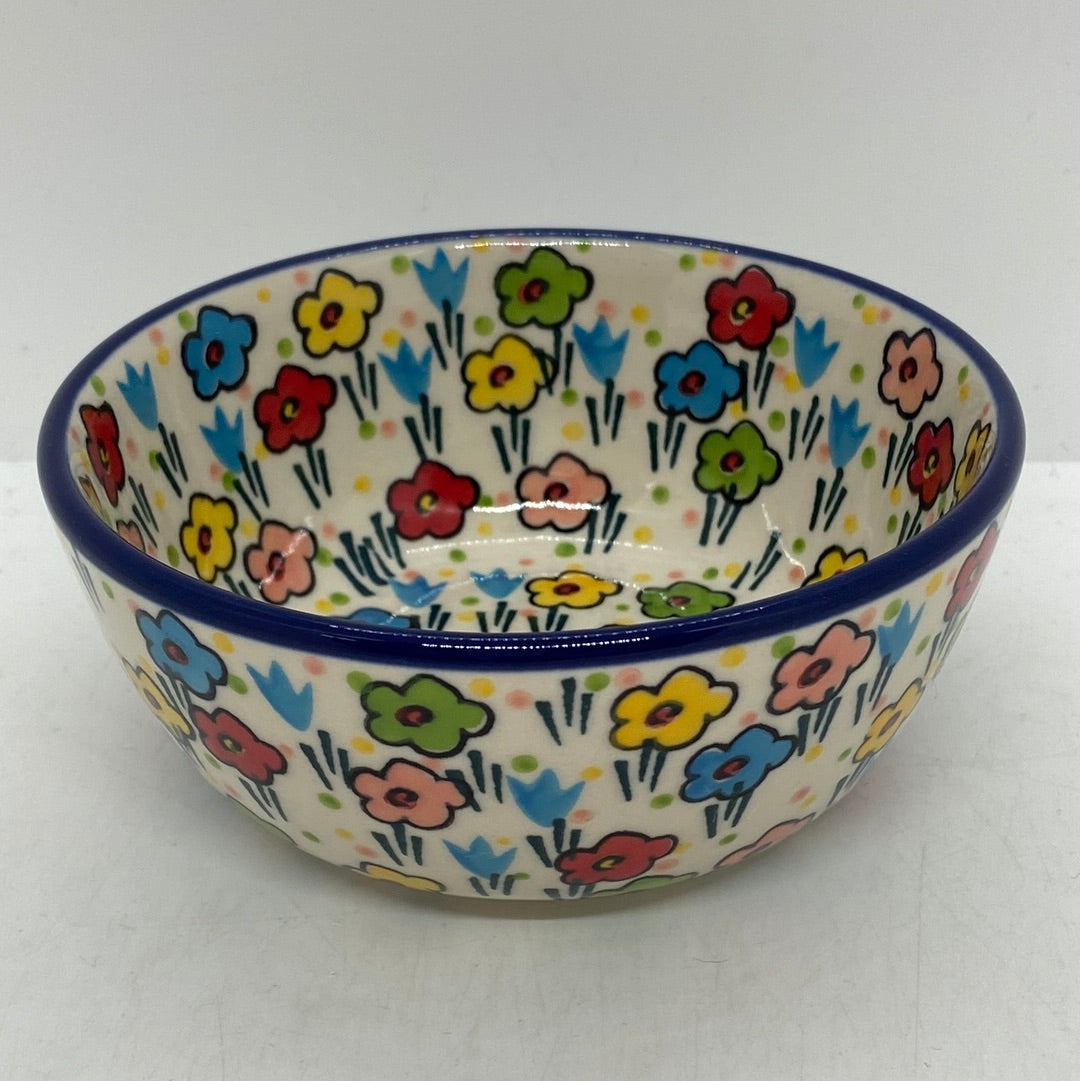 Slightly elevated view of a Ceramika Artystyczna Polish pottery bowl featuring a solid dark blue rim and hand-painted multi-colored spring flowers on both the cream-colored interior and exterior walls.