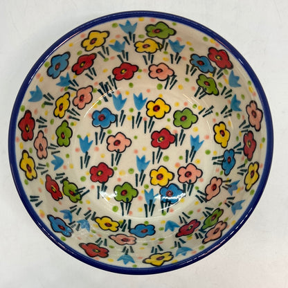 Top-down overhead view looking into a Ceramika Artystyczna Polish pottery bowl, showing a solid dark blue rim and a fully decorated interior featuring hand-painted multi-colored spring flowers on a cream background.