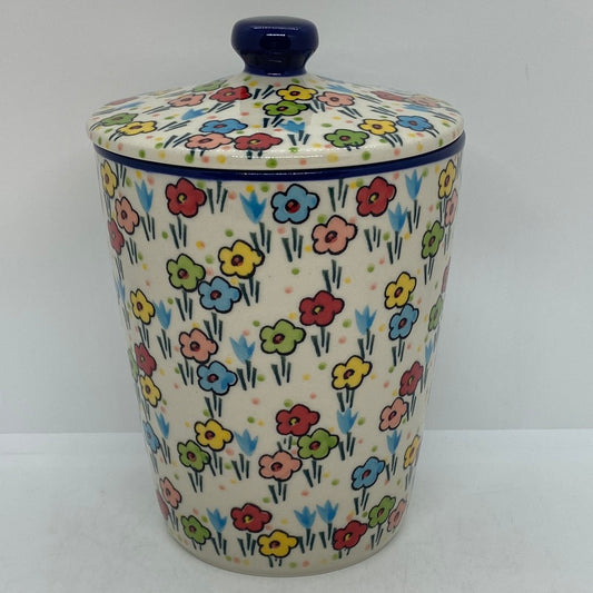 Front-facing view of a Ceramika Artystyczna Polish pottery tall canister with a lidded top, showing the dark blue knob and hand-painted spring floral pattern.