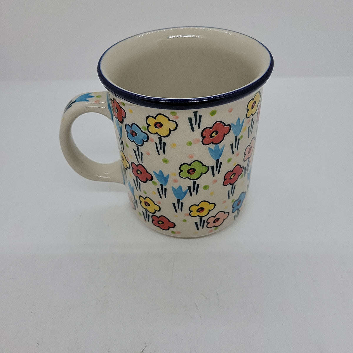 Angled view of a Ceramika Artystyczna Polish pottery coffee mug showing the interior rim, side handle, and hand-painted spring floral pattern.