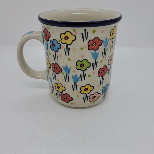 Front-facing view of a Ceramika Artystyczna Polish pottery coffee mug showing the side handle, dark blue rim, and hand-painted spring floral pattern