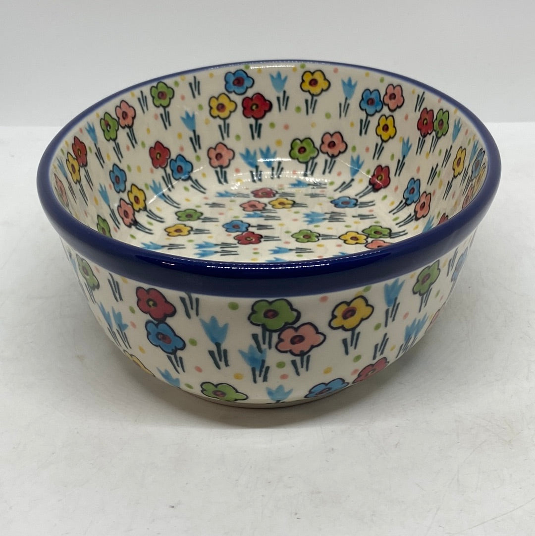 Slightly elevated angled view of a Ceramika Artystyczna Polish pottery deep round bowl, showing a solid dark blue rim and hand-painted multi-colored spring flowers covering both the interior and exterior.