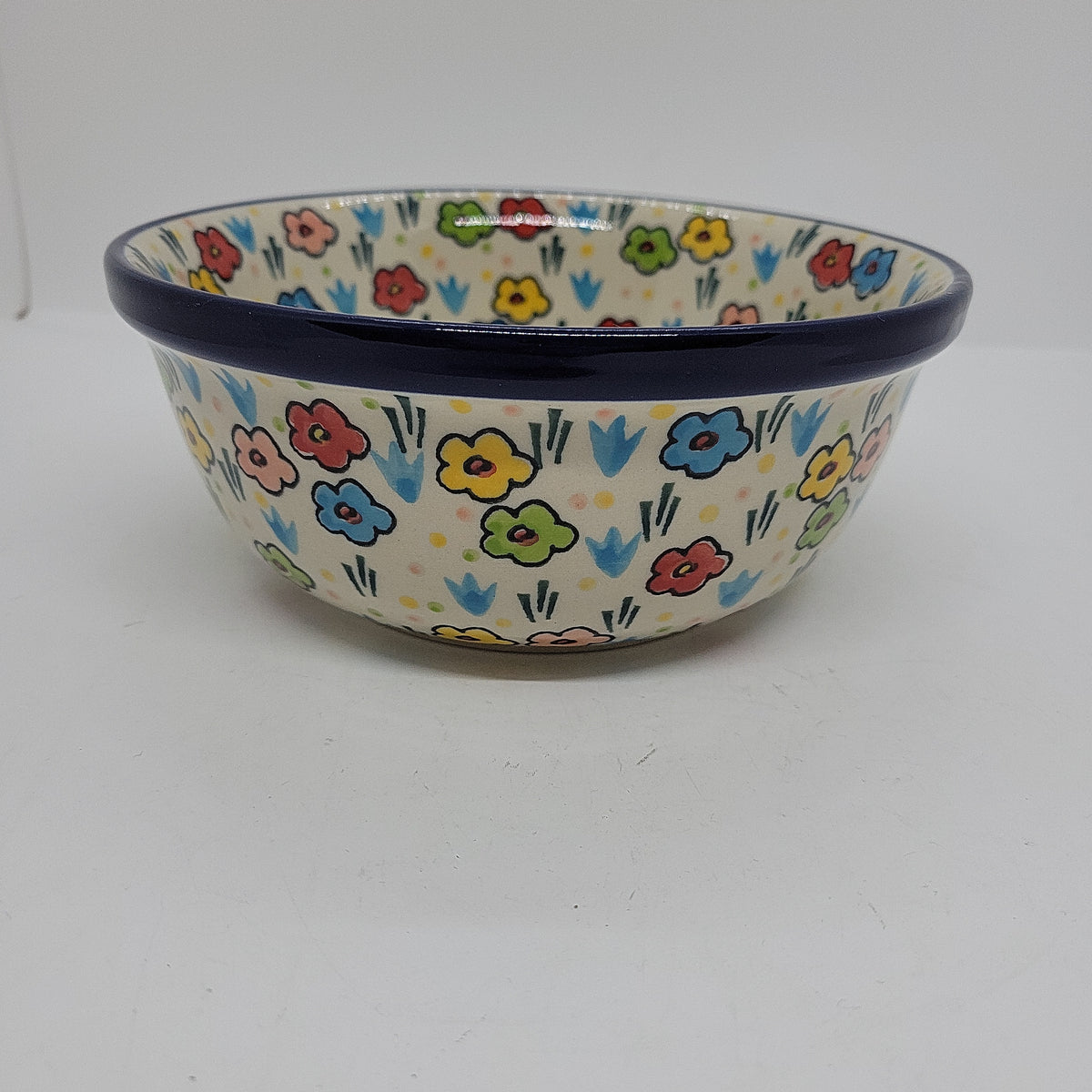 Slightly elevated side profile of a Ceramika Artystyczna Polish pottery bowl featuring a flared dark blue rim and hand-painted multi-colored spring flowers on the exterior and interior.