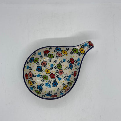 Top-down overhead view of a Ceramika Artystyczna Polish pottery handled spoon rest, showing a dark blue rim and hand-painted multi-colored spring flowers covering the basin and handle