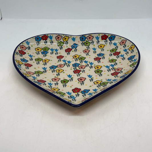 Angled view of a Ceramika Artystyczna Polish pottery heart platter showing the dark blue rim and hand-painted spring floral pattern.