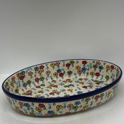 Elevated angled view of a Ceramika Artystyczna Polish pottery oval baking dish, featuring a dark blue rim and hand-painted multi-colored spring flowers completely covering the interior basin and exterior walls.