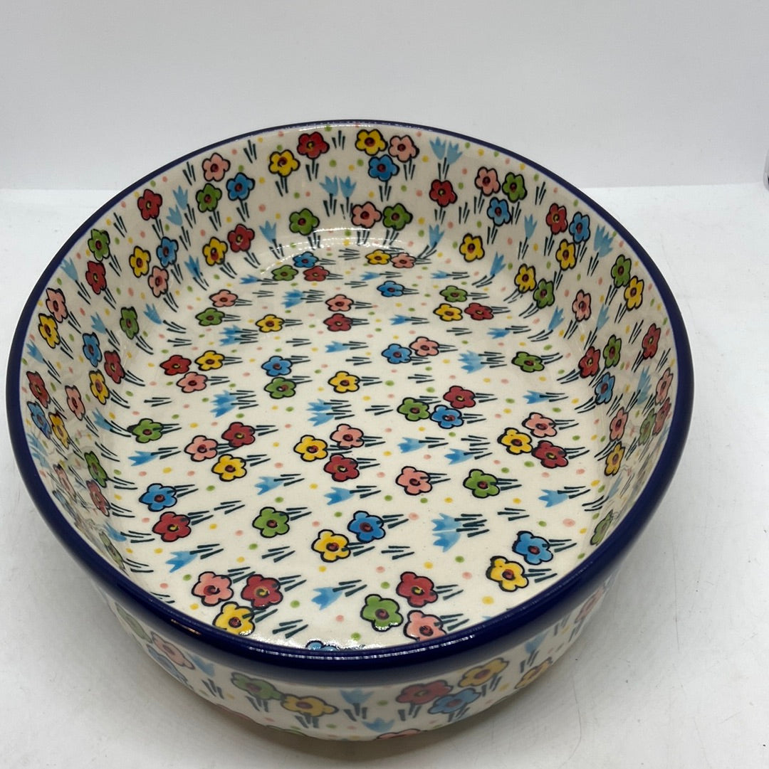 High-angle view looking into a Ceramika Artystyczna Polish pottery oval baker, showing a dark blue rim and hand-painted multi-colored spring flowers completely covering the flat interior floor and steep walls.