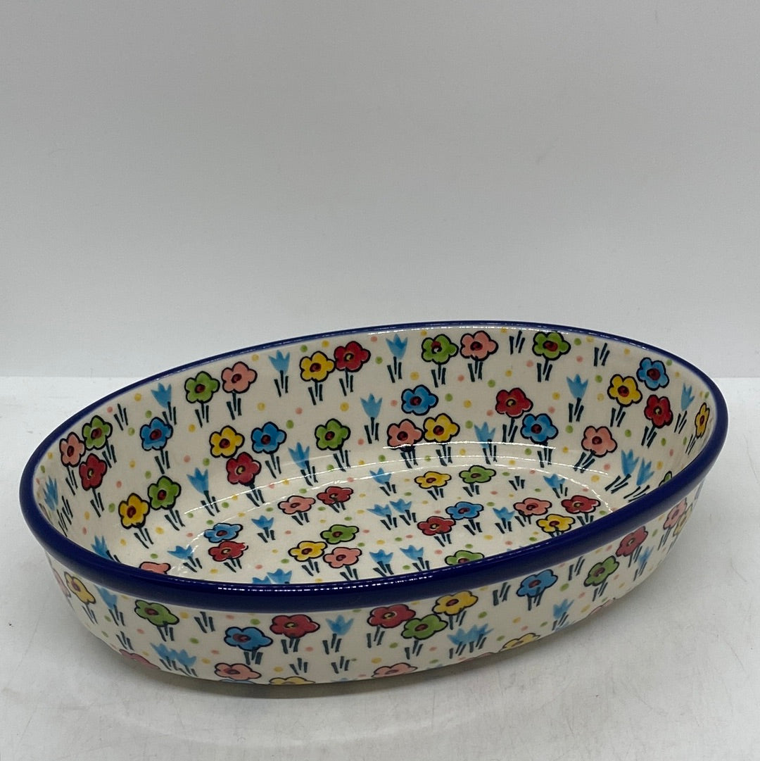 Slightly elevated angled view of a Ceramika Artystyczna Polish pottery deep oval baking dish, showing a solid dark blue rim and hand-painted multi-colored spring flowers covering both the interior basin and exterior walls.