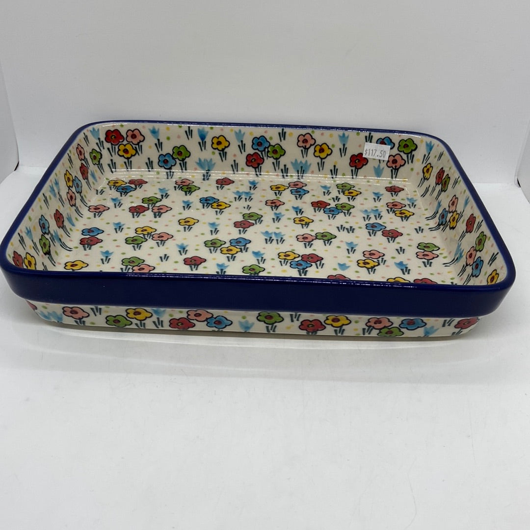 Angled view of a Ceramika Artystyczna Polish pottery large rectangular baking dish, showing a dark blue rim band, deep sides, and hand-painted spring flowers.