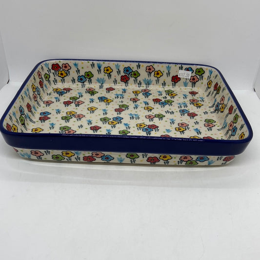 Angled view of a Ceramika Artystyczna Polish pottery large rectangular baking dish, showing a dark blue rim band, deep sides, and hand-painted spring flowers.