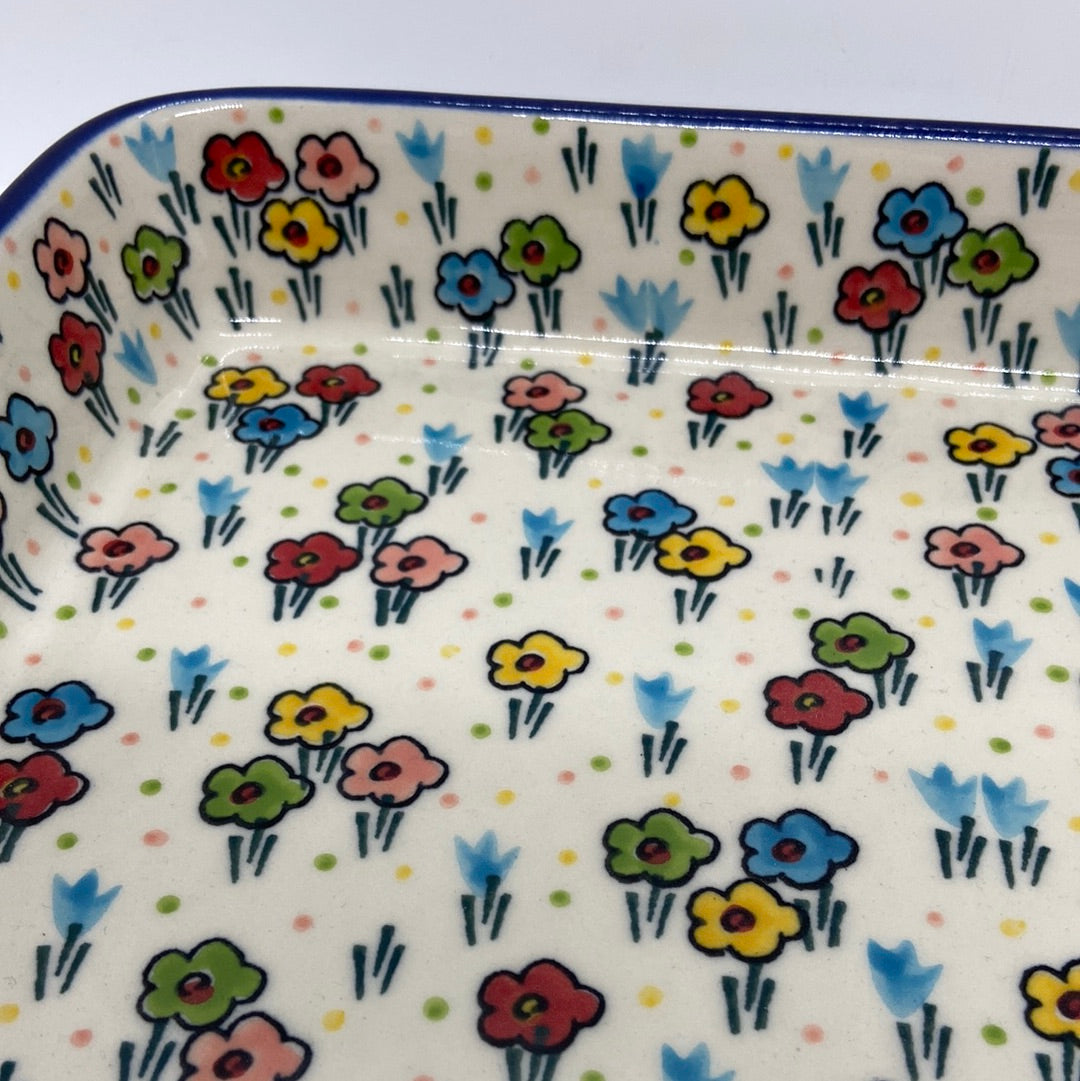 Macro close-up of a Ceramika Artystyczna Polish pottery large rectangular baking dish showing hand-painted spring flowers, green stems, and a glossy protective glaze.