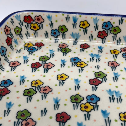 Macro close-up of a Ceramika Artystyczna Polish pottery large rectangular baking dish showing hand-painted spring flowers, green stems, and a glossy protective glaze.