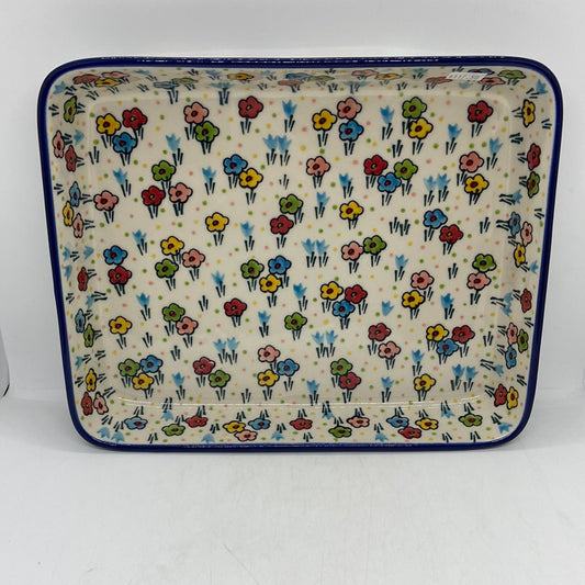 Direct overhead view of a Ceramika Artystyczna Polish pottery rectangular baking dish, showing a dark blue rim and hand-painted multi-colored spring flowers across the flat interior basin.