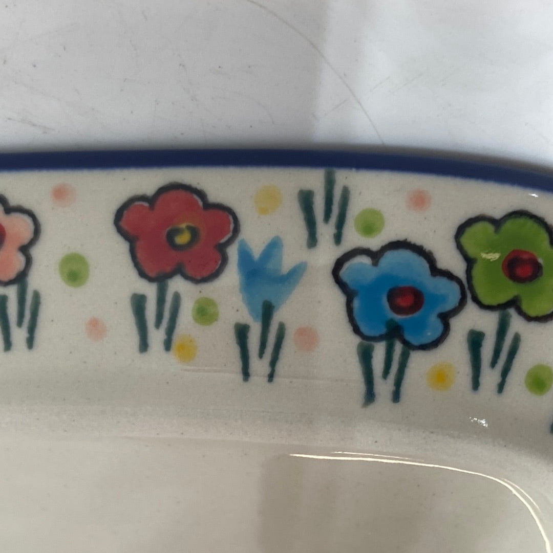 Close-up of the interior rim of a Ceramika Artystyczna Polish pottery tray, showing hand-painted multi-colored spring flowers on the sloping wall, a solid dark blue top edge, and a flat cream-colored bottom.