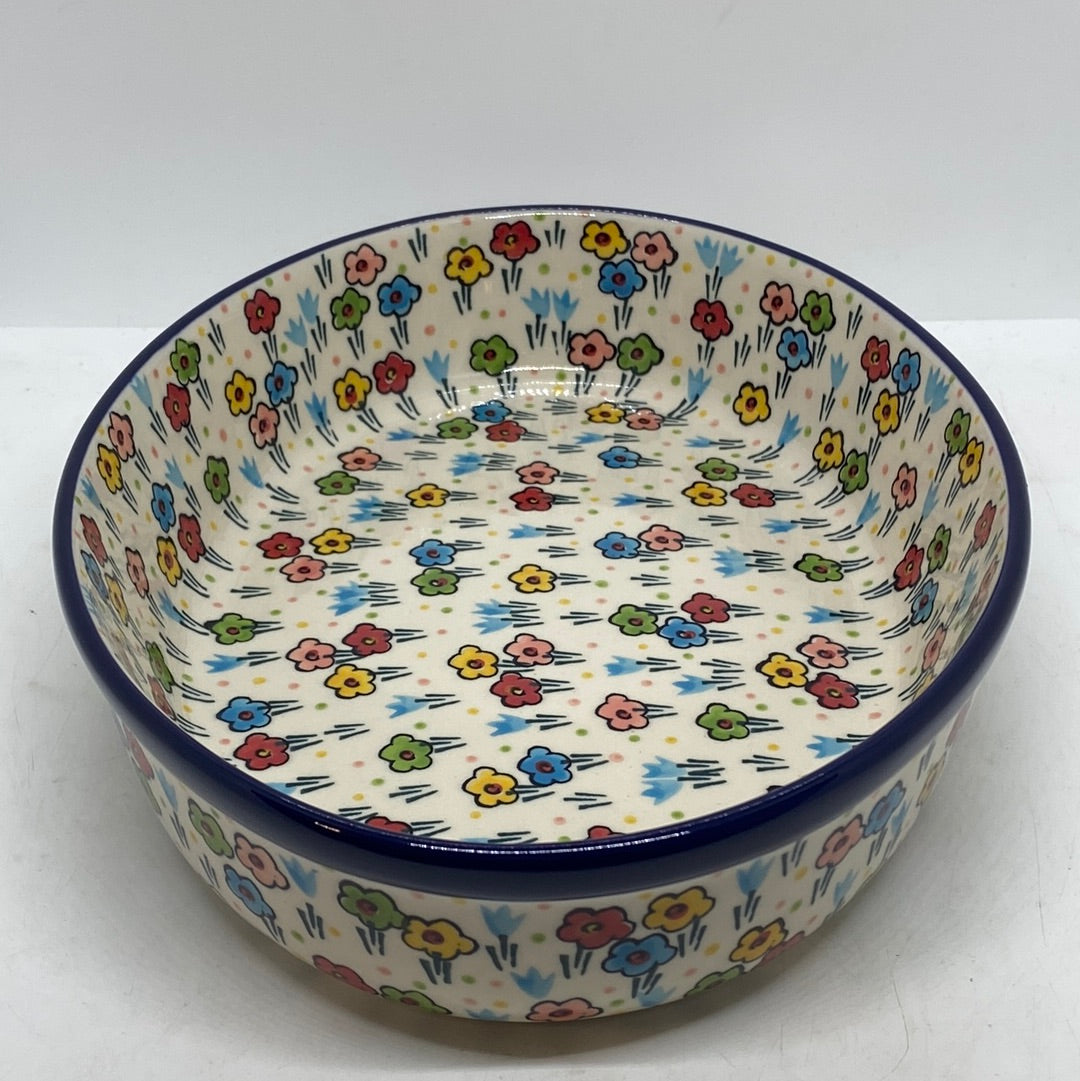 Elevated angled view of a Ceramika Artystyczna Polish pottery baker, featuring vertical walls, a flat interior basin, and hand-painted multi-colored spring flowers completely covering the inside and outside.